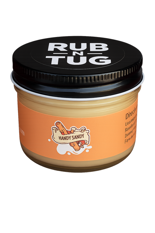 A close-up of the Rub N Tug "Handy Sandy" hair pomade jar, featuring a bold orange label with a playful cartoon log character gripping a banner that reads "Handy Sandy." The black lid prominently displays the Rub N Tug logo in white, and the glass jar rests against a smooth gradient background. Handy Sandy by Rub N Tug — a premium, all-natural pomade with cheeky branding and long-lasting hold, developed by barbers for confident, playful styling.