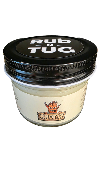 Photograph of a cylindrical glass jar of Rub N Tug pomade with a black lid displaying bold white text that reads “Rub N Tug.” The label features the “Knotty” variant, illustrated with a mischievous cartoon tree character gripping a wooden sign bearing the name “KNOTTY” in large block letters. The product is set against a solid black background, emphasizing its bold and edgy styling.
Organic men’s hair pomade, Knotty Rub N Tug styling product, matte hold grooming jar, veteran-owned natural hair care.