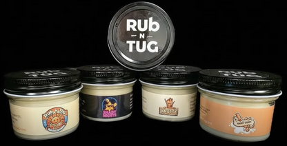 The Rub N Tug Pomade Collection lined up against a black background, featuring five unique glass jars with bold black lids and custom front labels: Sunset Dreams, Shady Nights, Knotty, Handy Sandy, and the original Rub N Tug logo jar on top. Each label reflects its own cheeky, vibrant personality, unified under the iconic Rub N Tug brand. Premium Rub N Tug hair pomade collection — all-natural, veteran-owned, barber-developed grooming line built for style, personality, and long-lasting hold.